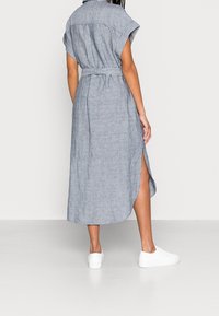 Robe midi rayée en bleu clair et blanc, en tissu léger. Dotée de manches courtes, d'une taille ceinturée et d'échancrures sur les côtés. Portée avec des baskets blanches.