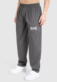 Grå ribbede sweatpants med elastisk talje, sidelommer og hvid "SMILODOX" logo trykt på venstre ben. Bæres med hvide sneakers.