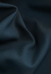 Tmavě modrá látka s jemnou strukturou, ukazující měkké záhyby a jemné stíny, které zdůrazňují její hladký a mírně lesklý povrch.