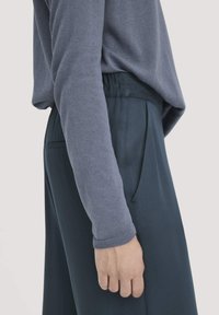 Lichtgrijze lange mouw top met textuurstof, gecombineerd met donkergroene wijde broek met zijzakken en een ontspannen pasvorm.