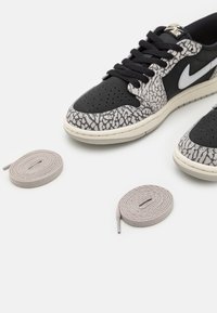 Baskets Nike Air noires et grises avec des accents imprimé éléphant et deux paires de lacets gris clair enroulés sur une surface blanche.