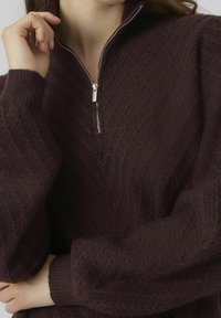 Maglione a maglia bordeaux con zip quarti, caratterizzato da motivi testurizzati e polsini a coste, che presenta un aspetto morbido e accogliente.