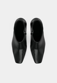 Botas de tornozelo pretas com um acabamento liso e brilhante, formato de bico fino e fechos de correr laterais. Textura suave com detalhes de design minimalistas.