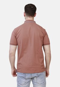 Polo shirt a maniche corte di colore ruggine con colletto a contrasto, realizzato in tessuto morbido, con vestibilità regolare e spacchi laterali nell'orlo.