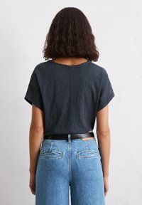Top corto grigio scuro con maniche corte e vestibilità comoda, abbinato a jeans in denim blu a vita alta con tasche posteriori e una cintura nera.