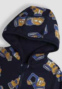 Felpa con cappuccio blu navy caratterizzata da ripetuti motivi di veicoli da costruzione gialli e blu. Realizzata in tessuto morbido con coulisse e zip frontale.