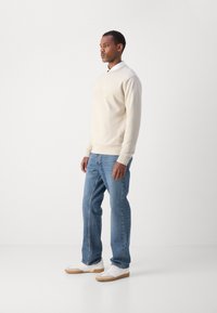 Sudadera crema con el logo "BOSS" en relieve, combinada con jeans de mezclilla azul y zapatillas blancas con suelas de goma. Diseño simple y casual.