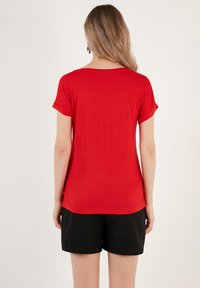Rød kortærmet t-shirt med rund halsudskæring, glat tekstur og en afslappet pasform, parret med sorte shorts.