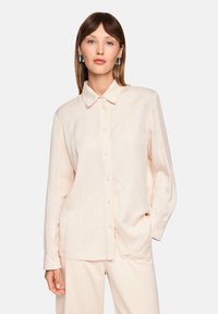 Light pink long-sleeve button-up shirt with a pointed collar, visible stitching details, and a relaxed fit. Features a soft, smooth texture.