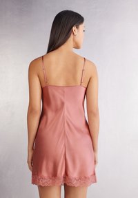 Sukienka z satyny w delikatnym odcieniu różu, z regulowanymi ramiączkami, prostym tyłem oraz koronkowym wykończeniem u dołu. Gładka tekstura.