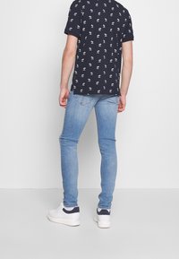 Marinblå kortärmad skjorta med vitt blommönster, matchad med ljusblå slim-fit jeans och vita sneakers med marinblå detaljer.