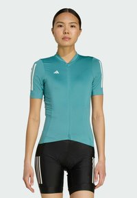 Turquoise cycling jersey with short sleeves and a front zipper, paired with black cycling shorts featuring white stripes on the sides.
