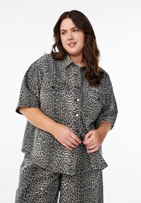 Chemise à manches courtes imprimée animal dans des tons sourds. Comprend deux poches poitrine, une fermeture à boutons sur le devant, et une coupe décontractée avec un ourlet arrondi.