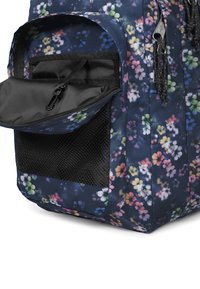 En blommönstrad ryggsäck i mörkblått, med en strukturerad mesh-framficka och ett zippered sidofack. Blommönster i olika färger.
