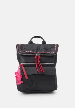 Sac à dos en cuir noir avec des tirettes de fermeture éclair rouges et un porte-clés personnage de dessin animé rose accroché à la fermeture éclair de la poche avant.