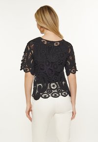 Sort blonde top med korte ærmer, der har indviklede paisley- og blomstermønstre. Delikat, struktureret materiale med en bølget kant.