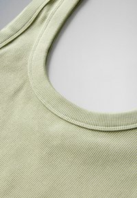 Light green ribbed fabric tank top neckline with visible stitching detail on a plain light background.