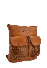 Sac à dos en cuir marron avec deux poches tissées à l'avant avec fermetures à rabat, fermeture éclair visible sur le dessus et bretelles réglables.