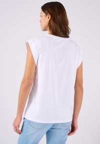 Top bianco a maniche corte in tessuto leggero con una vestibilità rilassata, caratterizzato da un collo rotondo e un delicato dettaglio di cucitura sulla parte posteriore.