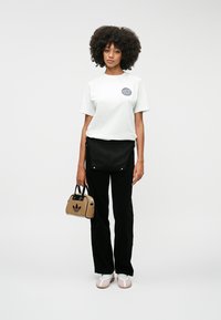 Biela tričko s okrúhlym modrým logom, čierne voľné nohavice a béžová kabelka s tmavým logom. Svetlohnedé topánky s bielymi akcentmi a textúrovaným dizajnom.