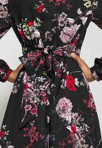 Robe noire à fleurs avec des fleurs rouges et rose clair, dotée d'une taille nouée et de manches froncées pour la texture et le détail.