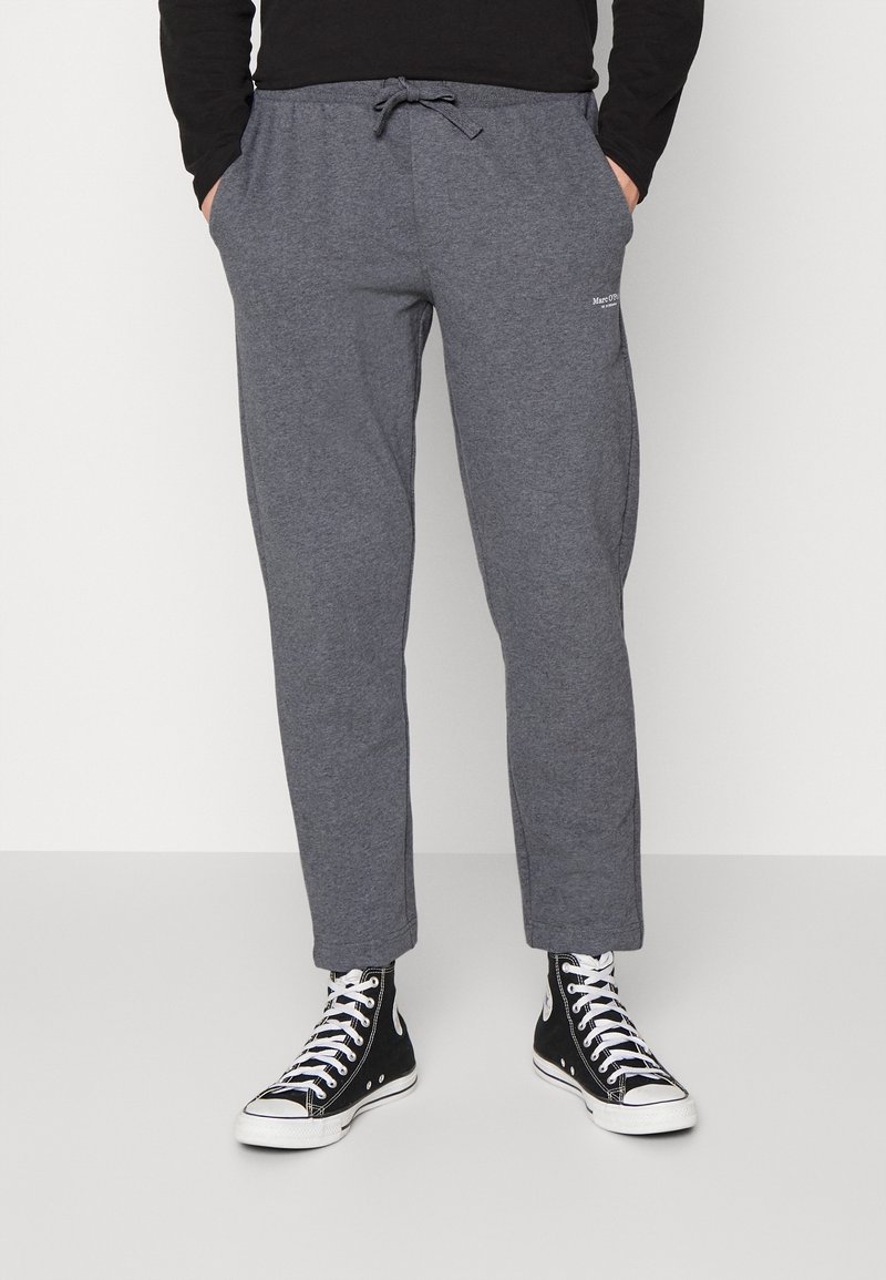 Graue Jogginghosen mit einem Kordelzugbund, tapered Beinen und Seitentaschen. Kombiniert mit schwarzen High-Top-Sneakern. Einfaches Logodesign vorhanden.