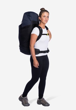 Zwarte en marineblauwe rugzak met verstelbare schouderbanden, een groot hoofdvak en een gevoerde heupriem, gedragen door een persoon in aansluitende kleding.