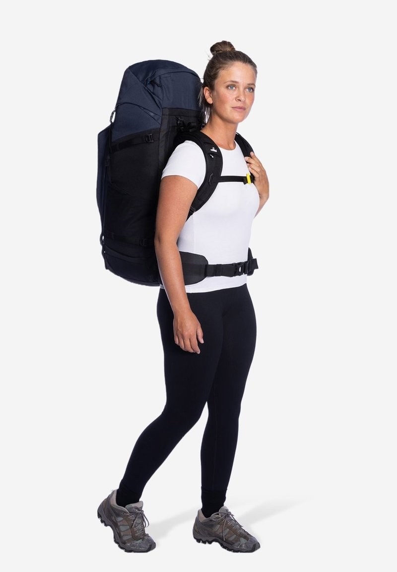 Zwarte en marineblauwe rugzak met verstelbare schouderbanden, een groot hoofdvak en een gevoerde heupriem, gedragen door een persoon in aansluitende kleding.