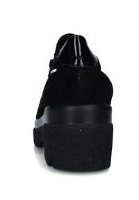 Scarpe in suede nero con un accento lucido in pelle verniciata sul tallone, caratterizzate da una suola nera spessa e texturizzata e un design minimalista.