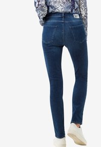 Vaqueros de denim azul delgado con cintura media y diseño de cinco bolsillos. Incluye bolsillos traseros y una textura suave.