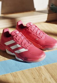 Pink athletic shoes with mesh upper, white stripes, textured detailing, rubber sole, and a rounded toe.