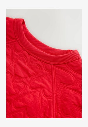 Tela acolchada roja con un patrón de corazones, con un escote acanalado. La textura parece suave, con detalles de costuras que delinean los corazones.