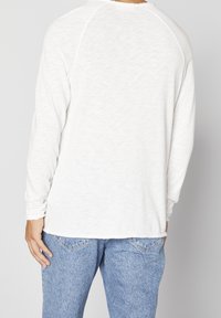 Vit långärmad skjorta med rundad fåll och subtil struktur, parat med blå högmidjade jeans med en klassisk femfickdesign.