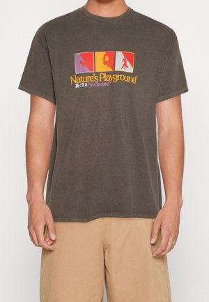 Braunes T-Shirt mit bunten Klettersilhouetten und dem Text "Nature's Playground", getragen mit beigen Shorts.
