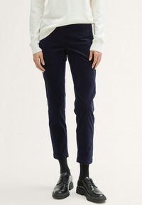 Navyblauwe corduroy broek met een getailleerde pasvorm, taps toelopende pijpen, een vlakke voorkant en zijzakken, gecombineerd met zwarte veterschoenen.