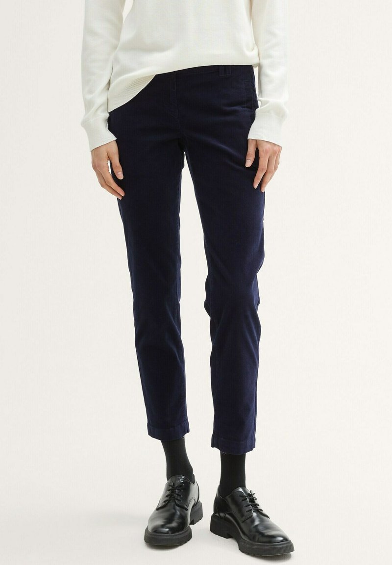 Navyblauwe corduroy broek met een getailleerde pasvorm, taps toelopende pijpen, een vlakke voorkant en zijzakken, gecombineerd met zwarte veterschoenen.