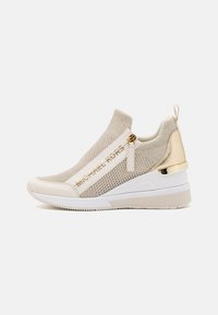 Sneakers slip-on in maglia beige con dettagli dorati e una spessa suola bianca, dotati di pannelli in rete e un ornamento con logo sul lato.