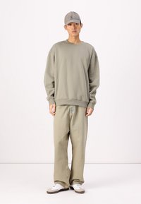 Sweatshirt surdimensionné vert clair et pantalon large vert pâle. Casquette de baseball grise. Baskets blanches avec des accents marron. Look simple et décontracté.