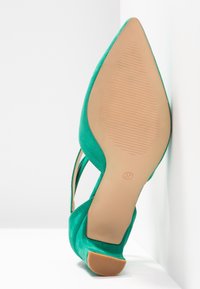Chaussure à talon haut verte à bout pointu reposant sur le dos, montrant la semelle beige texturée avec la marque de taille 37.