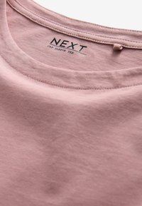 T-shirt à manches courtes en tissu rose doux, avec un col rond agrémenté de coutures et d'une étiquette de marque au niveau du col.