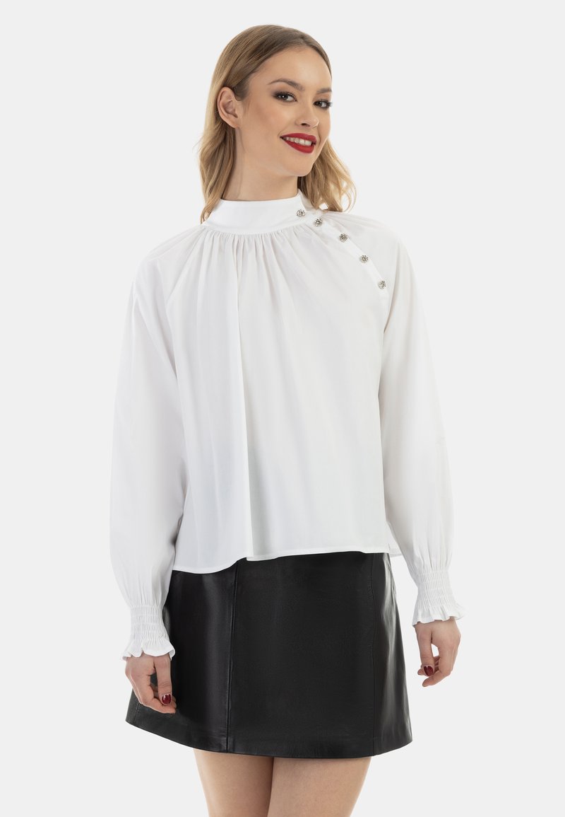 Hvid bluse med højt halsudskæring, plisseret design og dekorative knapper på den ene side, parret med en sort læder mini-nederdel.