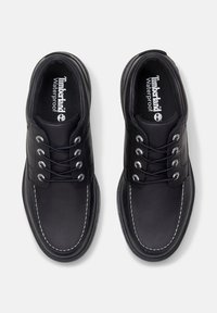 Schwarze wasserdichte Schuhe mit einer glatten Lederoberfläche, runder Zehenpartie, kontrastierender weißer Naht und metallischen Ösen für die Schnürsenkel.