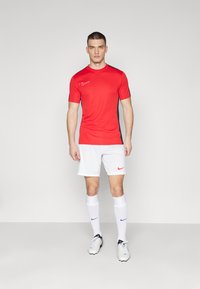 Rotes Kurzarmtrikot mit schwarzen Akzenten, kombiniert mit weißen Shorts. Das Nike-Logo ist auf beiden Teilen, zusammen mit weißen Socken und Fußballschuhen.