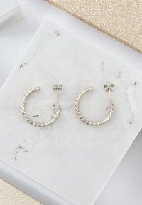 Silver twist hoops med en texturerad yta, med en säker stift- och baksidesstängning. Visade på en marmoryta.