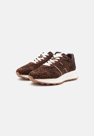 Ζευγάρι καφέ sneakers με λεοπάρ σχέδιο, λευκά κορδόνια και χοντρές λευκές σόλες σε απλό ανοιχτό φόντο.