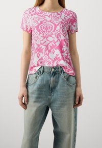 Top de manga corta rosa y blanco con un patrón floral, combinado con jeans de tiro alto en azul claro que tienen bolsillos delanteros y un corte relajado.