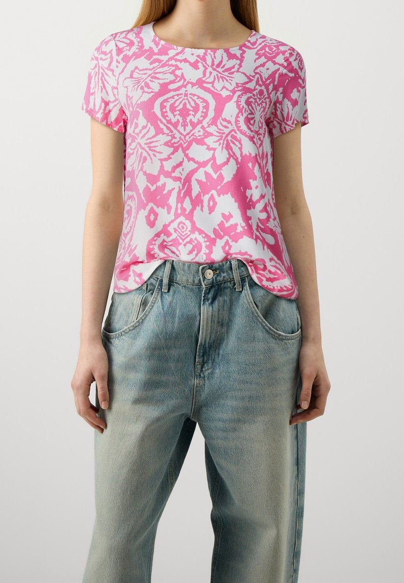 Top de manga corta rosa y blanco con un patrón floral, combinado con jeans de tiro alto en azul claro que tienen bolsillos delanteros y un corte relajado.