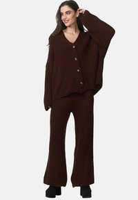 Ensemble en deux pièces en tricot côtelé brun comprenant un cardigan oversize à col en V avec cinq boutons et un pantalon à jambes larges avec une finition texturée.