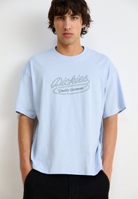 Šviesiai mėlynas medvilninis marškinėliai trumpomis rankovėmis, su grafiniu logotipu "Dickies" ir "Quality Garments" kontrastinga tamsia spalva.