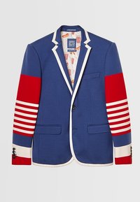 Blazer bleu avec bordure blanche, patchs rayés rouges et blancs sur les manches, et doublure à motif pop-corn visible à l'intérieur du col.
